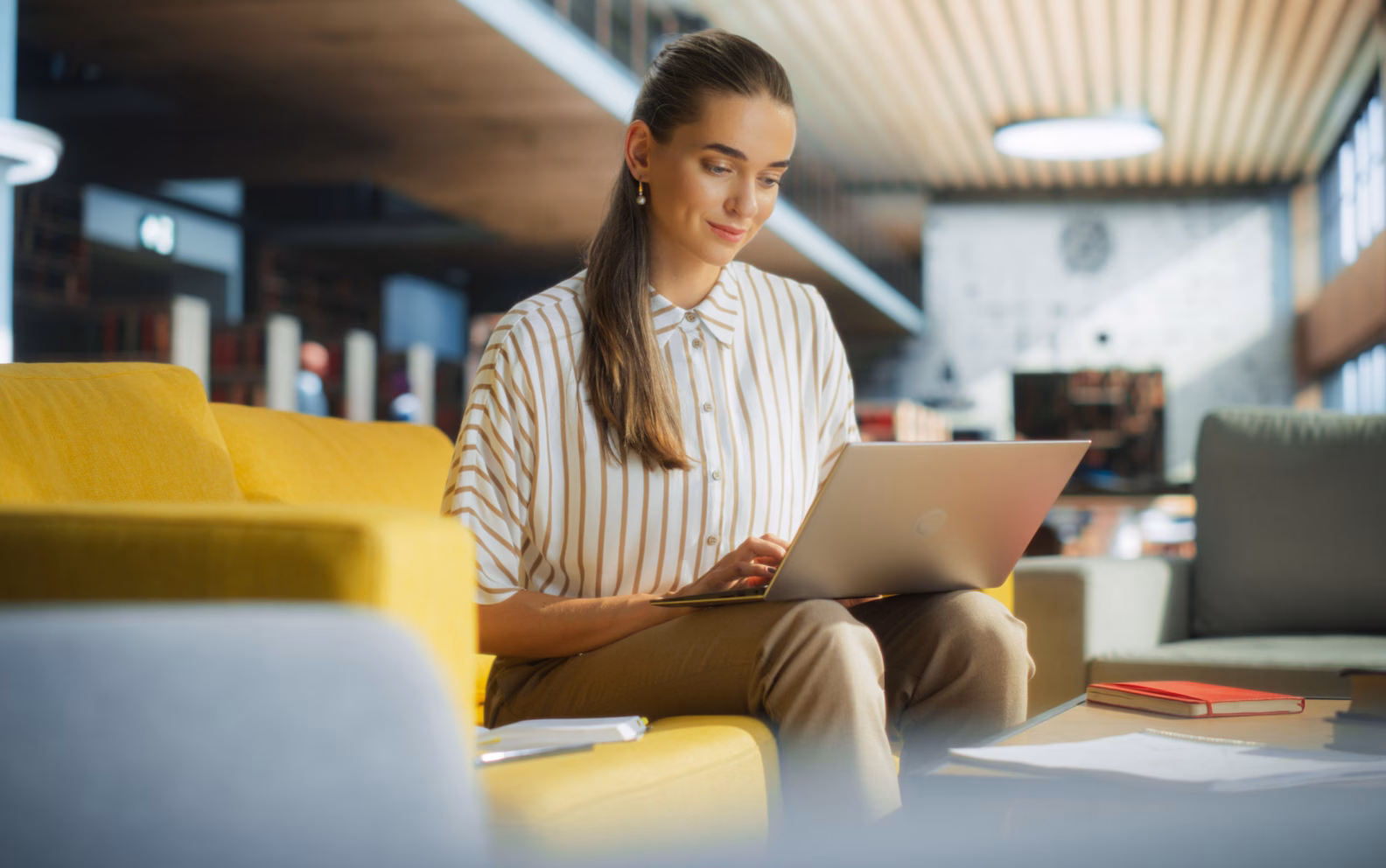 Image shows a woman seated in a hotel lobby working on her laptop